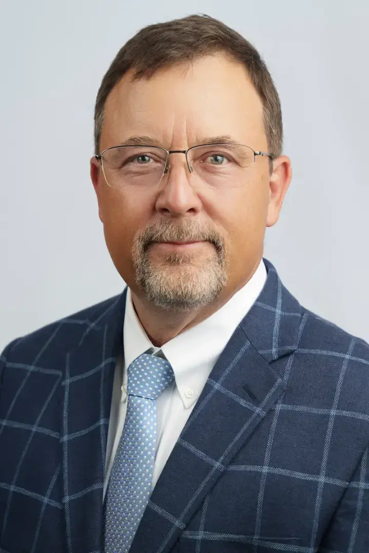 Portrait of a middle-aged man with glasses in a blue plaid suit and light blue tie, looking at the camera.